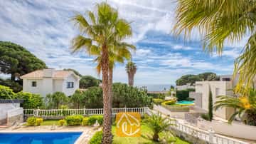 Buitenaanzicht vanaf Villa Estrella met een zwembad op de voorgrond, palmbomen, witte balustrades en naburige villa's onder een blauwe lucht met her en der wat wolken.