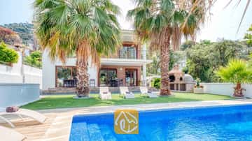 Privézwembad met blauwe mozaïektegels en ligstoelen op het gras bij Villa Marcella, omgeven door palmbomen en voorzien van een stenen barbecue.