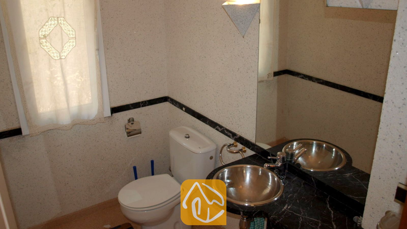 Compacte badkamer met een wit toilet, een zwart marmeren wastafelblad met een ronde metalen waskom, en een matglasraam met een gedessineerd gordijn.