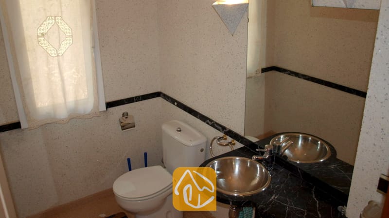 Compacte badkamer met een wit toilet, een zwart marmeren wastafelblad met een ronde metalen waskom, en een matglasraam met een gedessineerd gordijn.