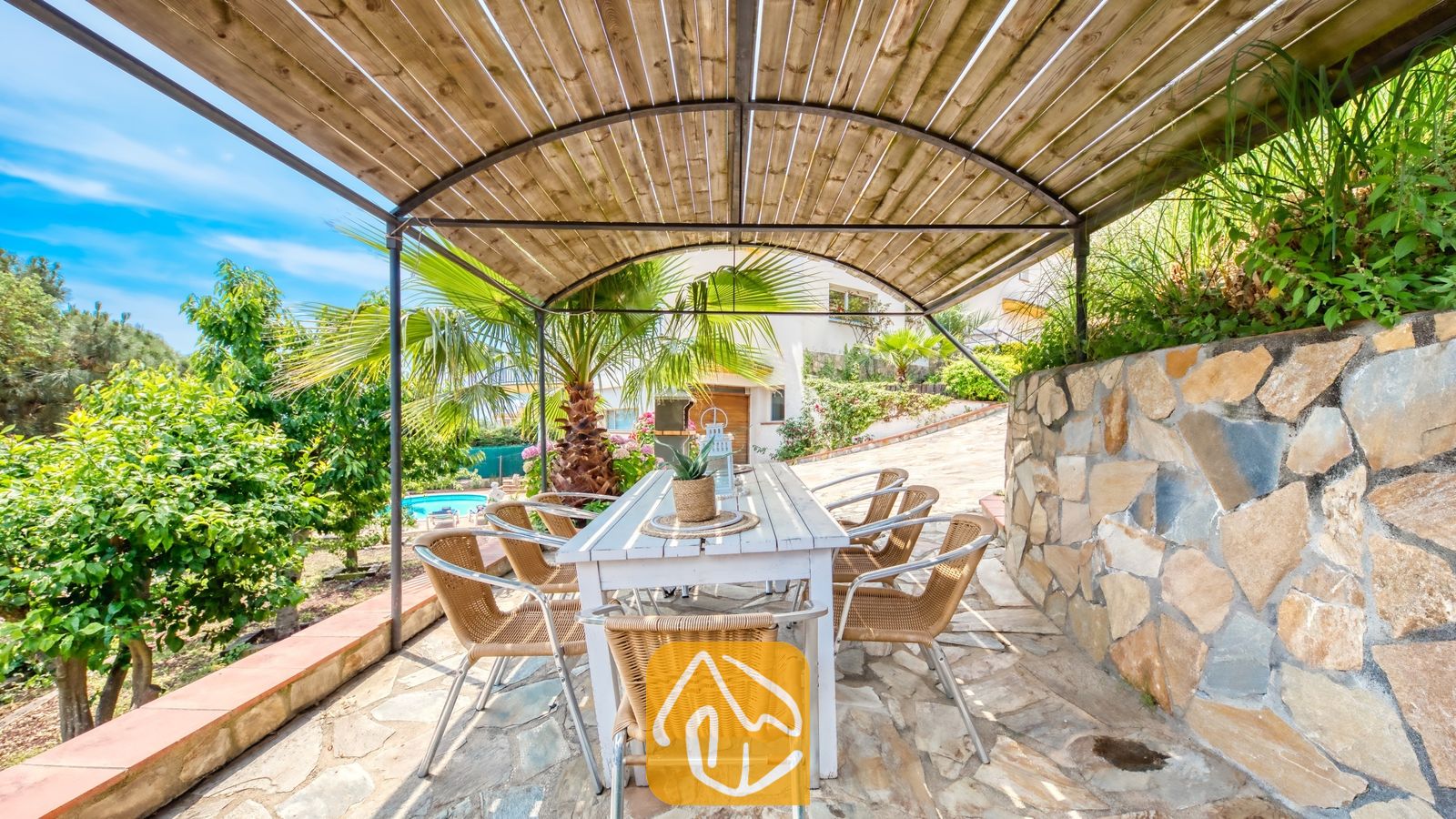 Overdekte buiten-eethoek bij Villa Valentina met een lange witte houten tafel en geweven rieten stoelen onder een gebogen houten pergola van latten.