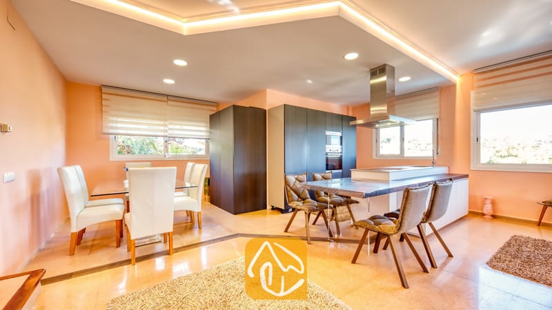 Moderne keuken en eethoek in Villa Valentina met donkere kasten, een glazen eettafel met witte stoelen en een kookeiland met gestoffeerde bruine stoelen.