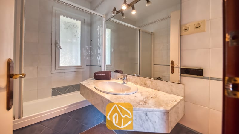 Badkamer voorzien van een wastafelmeubel met marmeren blad en een grote wandspiegel, een ligbad met glazen wand en witte wandtegels.