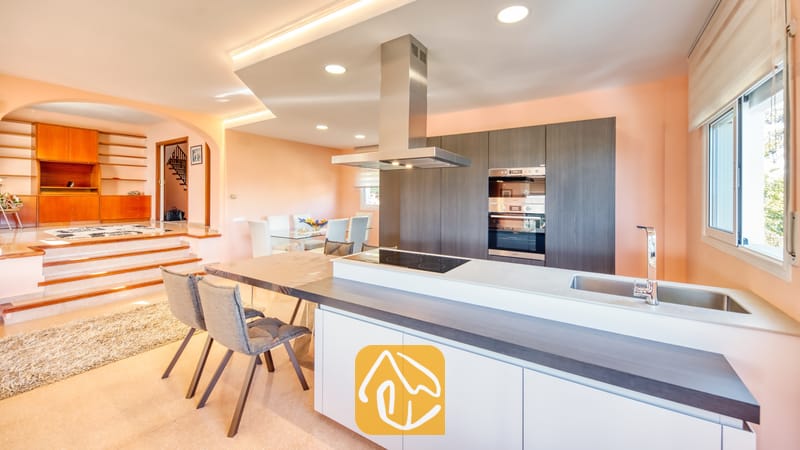 Moderne keuken met donkere houten kasten, een roestvrijstalen afzuigkap en een aangrenzende eethoek met een trap naar een verhoogde woonkamer.