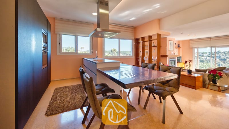Moderne keuken en eethoek met een glazen eettafel, gestoffeerde stoelen en een rvs-afzuigkap.