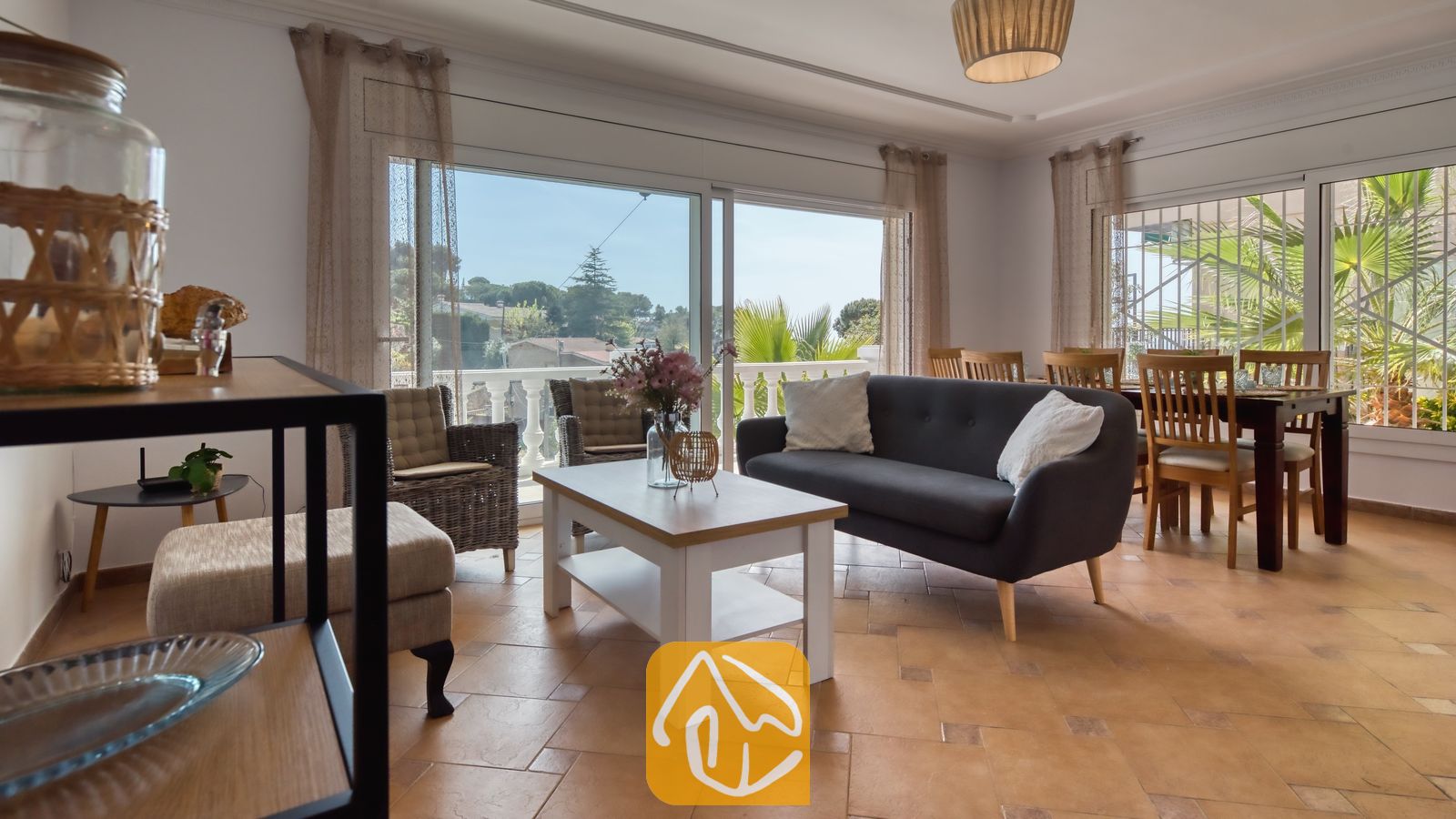 Woonkamer van Villa Donna met een donkergrijze bank, een witte salontafel en grote glazen schuifdeuren die opengaan naar een balkon met uitzicht naar buiten.