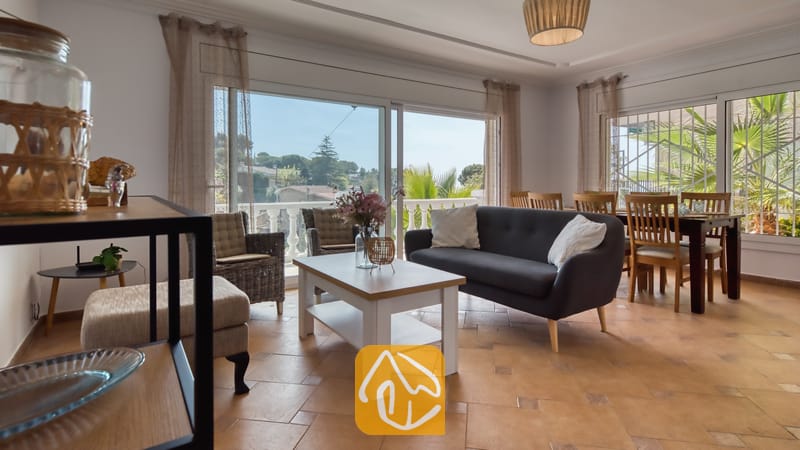 Woonkamer van Villa Donna met een donkergrijze bank, een witte salontafel en grote glazen schuifdeuren die opengaan naar een balkon met uitzicht naar buiten.