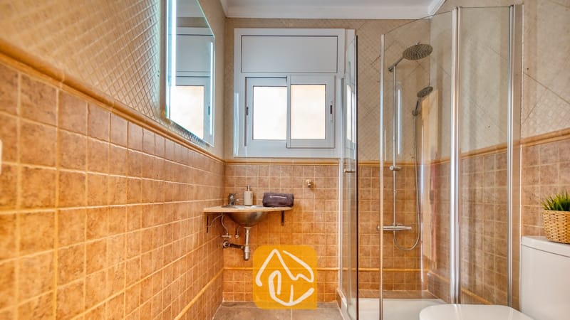 Badkamer voorzien van beige vierkante wandtegels, een glazen inloopdouche met twee douchekoppen en een wastafel.