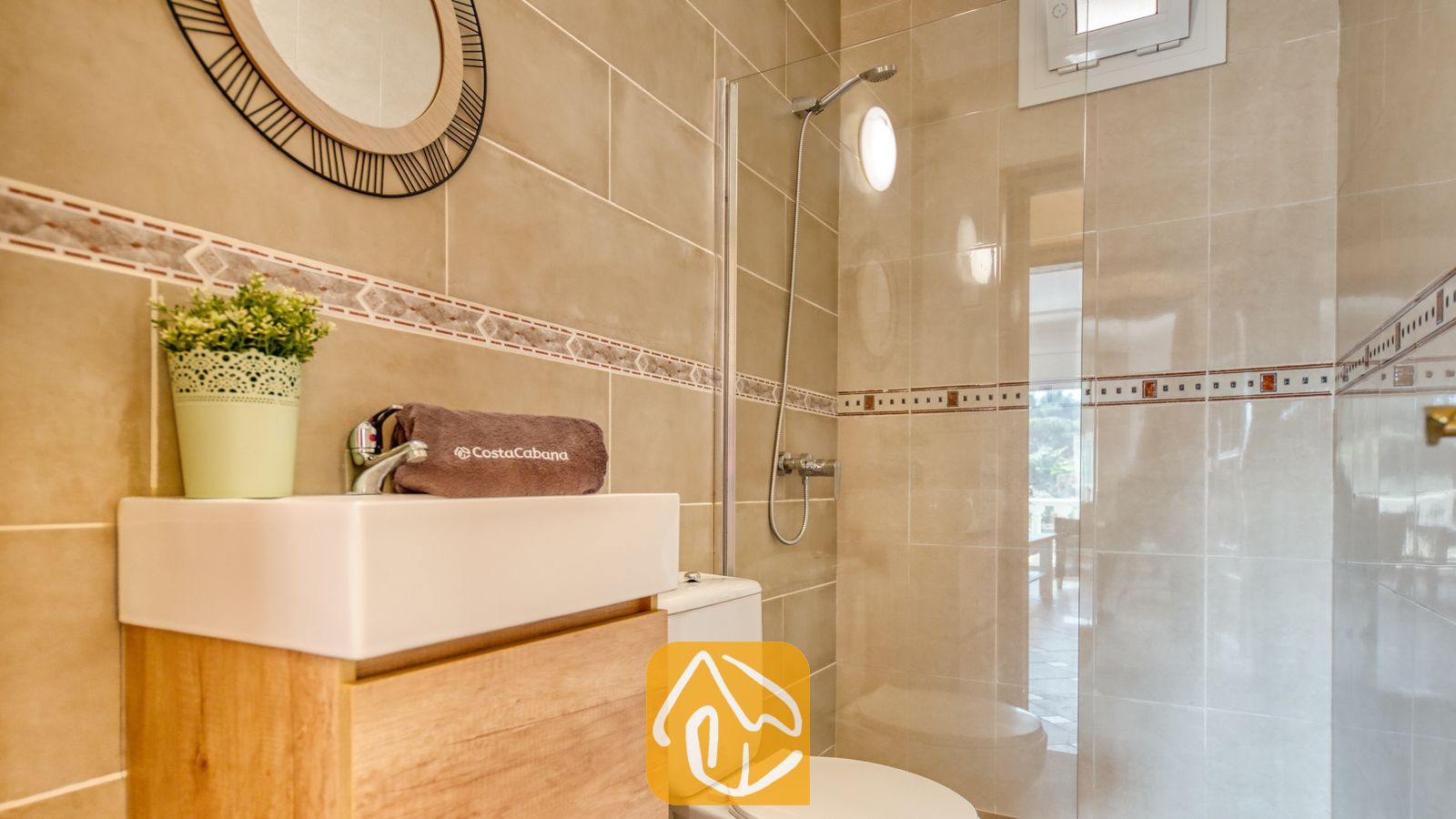 Moderne badkamer met betegelde muren in een beigetint, een houtenwastafelmeubel met een witte waskom, een ronde decoratieve spiegel en een glazen inloopdouche.