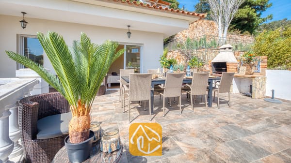 Zonnig terras bij Villa Donna, voorzien van een eettafel voor buiten met rieten stoelen, een ingebouwde stenen barbecue en betegelde vloeren.