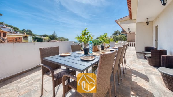 Terras van Villa Donna met een donkere eettafel en geweven rotan stoelen, gedekt met borden en potten met citroenboompjes onder een blauwe hemel.