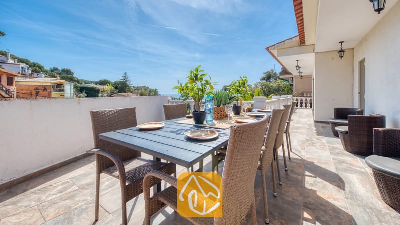 Terras van Villa Donna met een donkere eettafel en geweven rotan stoelen, gedekt met borden en potten met citroenboompjes onder een blauwe hemel.