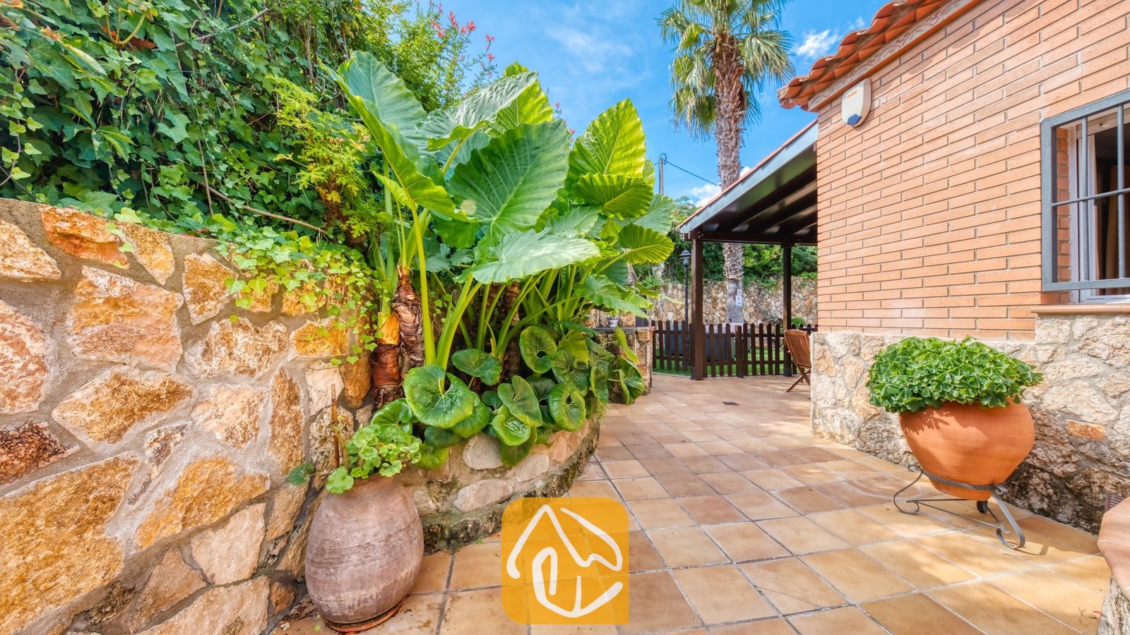 Binnenplaats van Villa Alba met een betegeld terras, grote tropische groene planten en een rustieke stenen muur.
