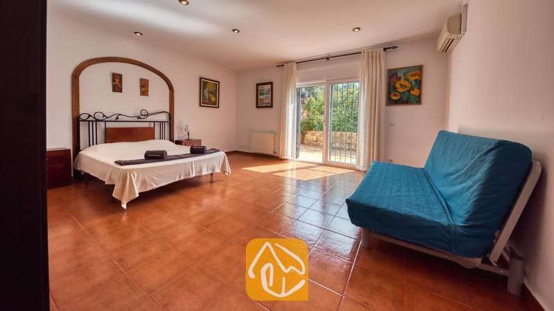 Ruime slaapkamer in Villa Alba met een tweepersoonsbed, een donker metalen frame, een blauwe bank en glazen schuifpui die toegang biedt tot een buitenterras.