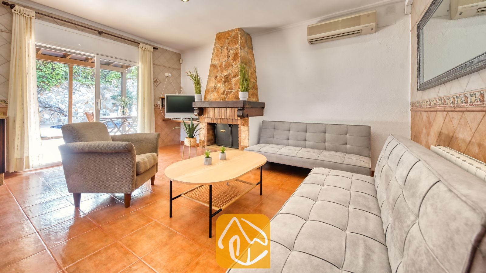 Woonkamer van Villa Alba met twee grijze Chesterfield-banken, een fauteuil, een ovale houten salontafel en een stenen open haard.