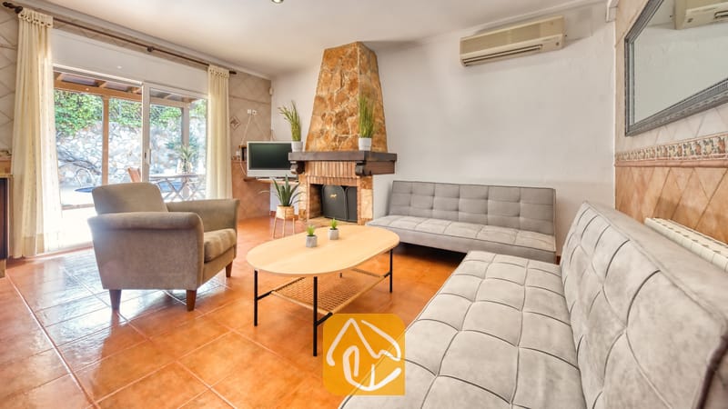 Woonkamer van Villa Alba met twee grijze Chesterfield-banken, een fauteuil, een ovale houten salontafel en een stenen open haard.