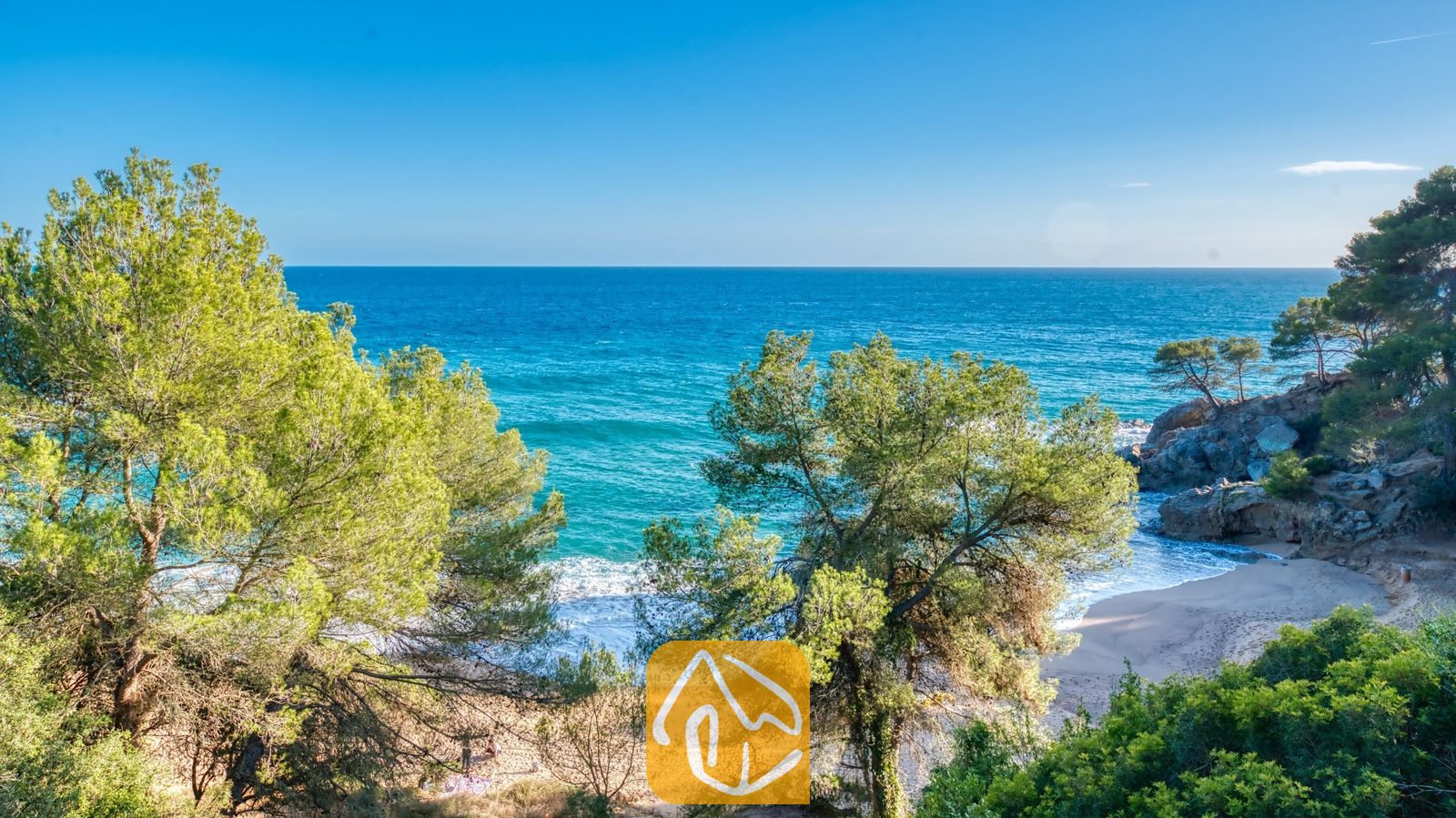 Een afgelegen zandbaai, omlijst door groene dennenbomen nabij Villa Santa Cristina, met azuurblauw zeewater en rotsachtige kliffen onder een stralende hemel.