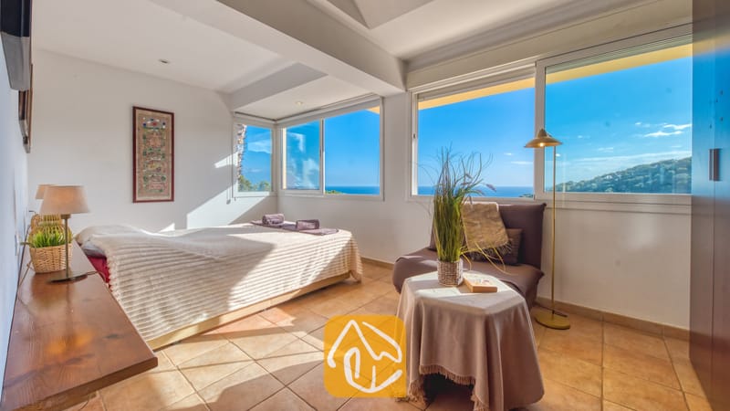 Slaapkamer in Villa Santa Cristina met een tweepersoonsbed, terracotta vloertegels en grote ramen die uitkijken over de zee en de heuvels langs de kust.