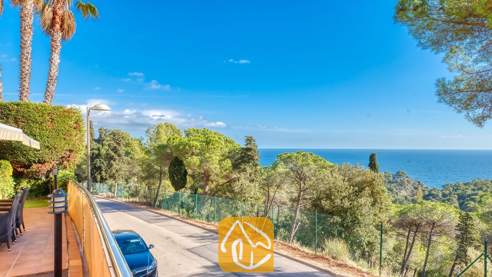 Kustpanorama vanaf Villa Santa Cristina met een geplaveide weg omzoomd door pijnbomen en een helder uitzicht op de blauwe zee in de verte.
