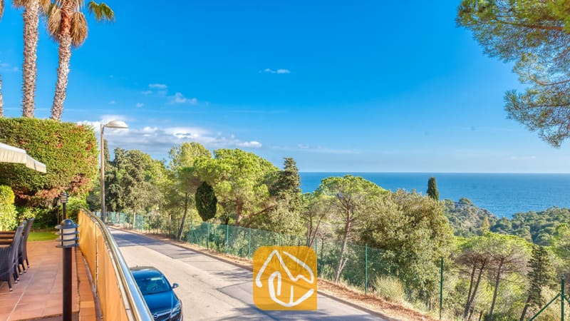 Kustpanorama vanaf Villa Santa Cristina met een geplaveide weg omzoomd door pijnbomen en een helder uitzicht op de blauwe zee in de verte.