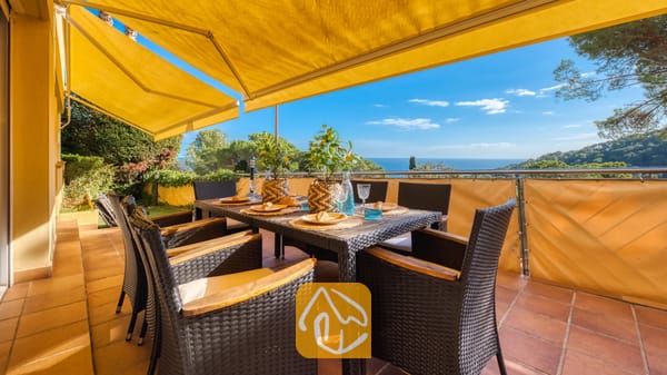 Terras met uitzicht op zee bij Villa Santa Cristina, voorzien van een eettafel voor zes personen, gele uitvalschermen en een vloer van terracotta tegels.