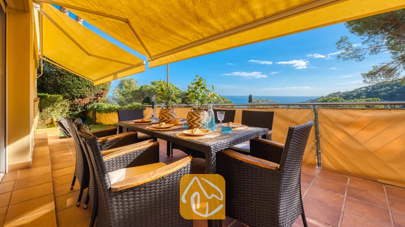 Terras met uitzicht op zee bij Villa Santa Cristina, voorzien van een eettafel voor zes personen, gele uitvalschermen en een vloer van terracotta tegels.