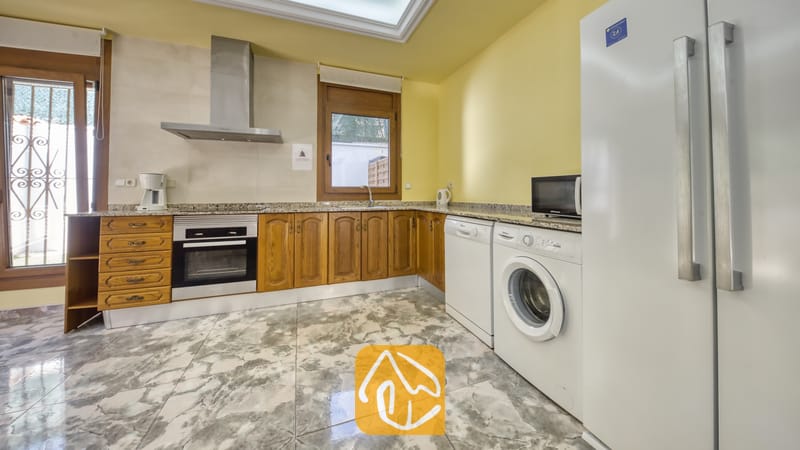 Keuken van Villa Baileys met houten kasten, marmeren aanrechtbladen, roestvrijstalen apparatuur en een wasmachine.