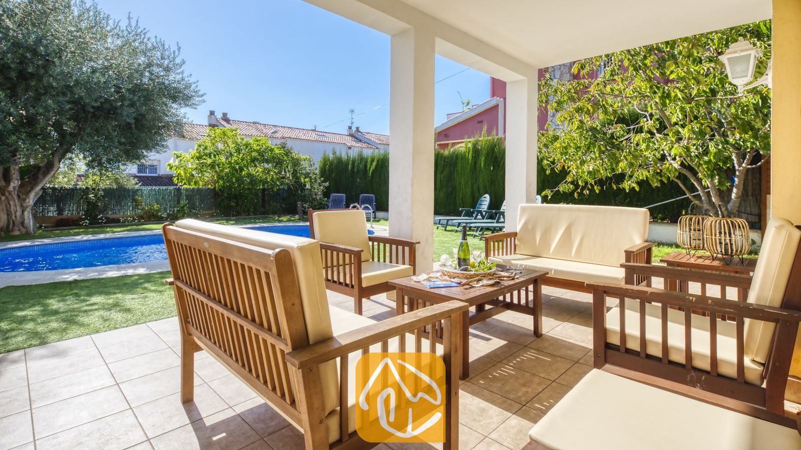Overdekt terras bij Villa Baileys met houten tuinmeubelen, crèmekleurige kussens en uitzicht op het zwembad en de tuin.