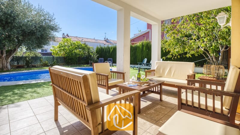 Overdekt terras bij Villa Baileys met houten tuinmeubelen, crèmekleurige kussens en uitzicht op het zwembad en de tuin.