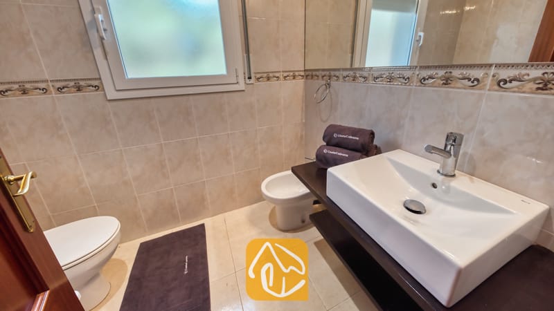 Een witte waskom op een donker wastafelmeubel in een badkamer van Villa Chanel, voorzien van beige wandtegels, een bidet en een matglazen raam.