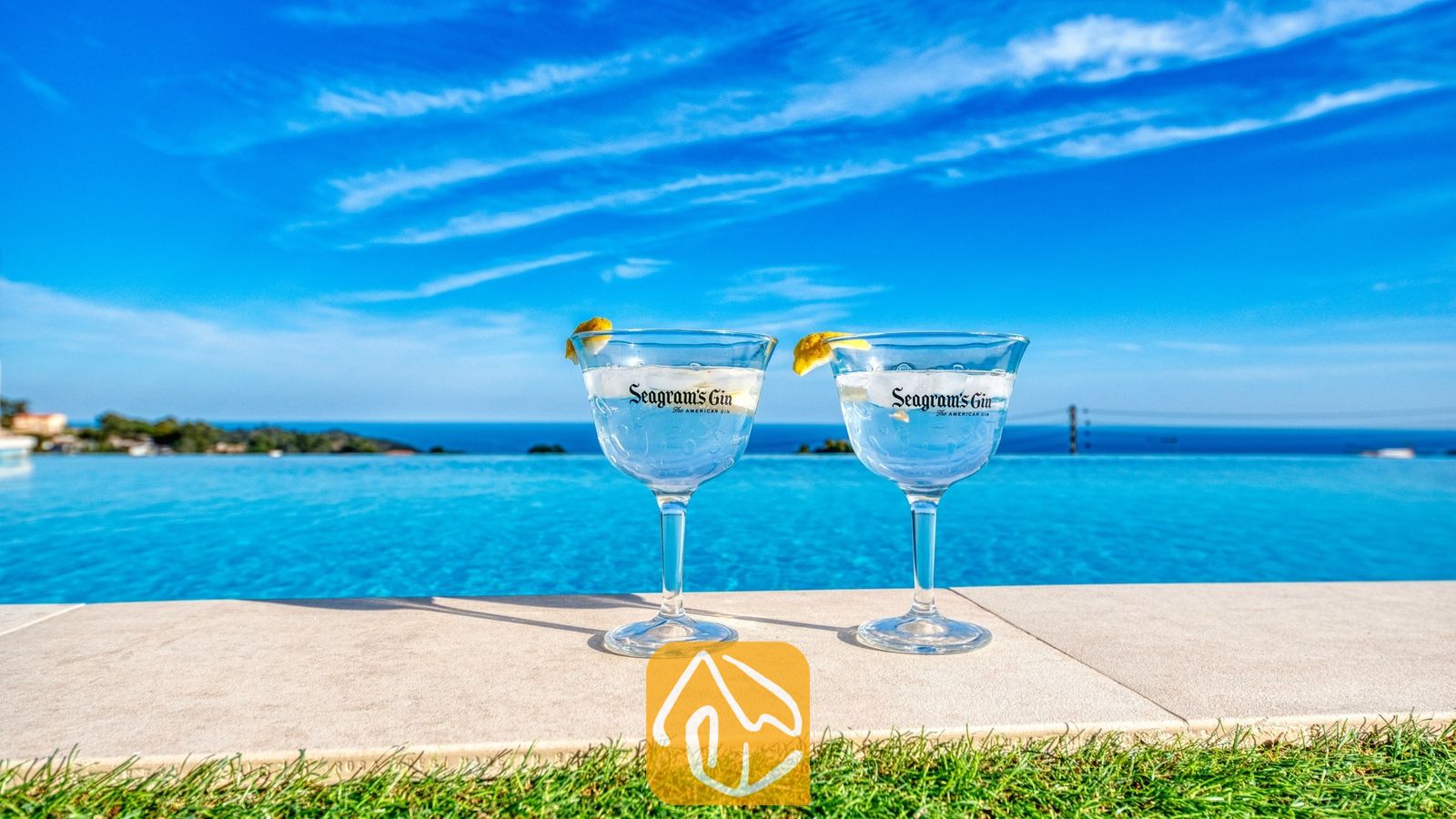 Twee gin-cocktails met citroengarnituur aan de rand van het overloopzwembad van Villa Chanel, met uitzicht op de blauwe zee en de lucht.