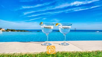 Twee gin-cocktails met citroengarnituur aan de rand van het overloopzwembad van Villa Chanel, met uitzicht op de blauwe zee en de lucht.