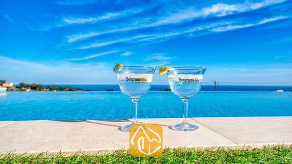 Twee gin-cocktails met citroengarnituur aan de rand van het overloopzwembad van Villa Chanel, met uitzicht op de blauwe zee en de lucht.