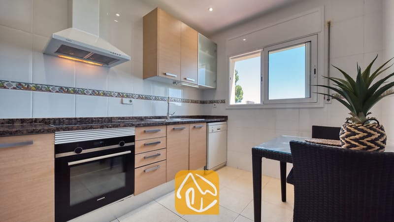 De keuken van Villa Chanel is voorzien van lichthouten kasten, een zwarte Siemens-oven en een kleine eettafel met donkere rieten stoelen bij het raam.