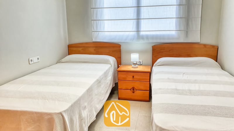Slaapkamer met twee eenpersoonsbedden voorzien van houten hoofdborden, wit gestreept beddengoed en een centraal nachtkastje met een klein lampje in Villa Chanel.