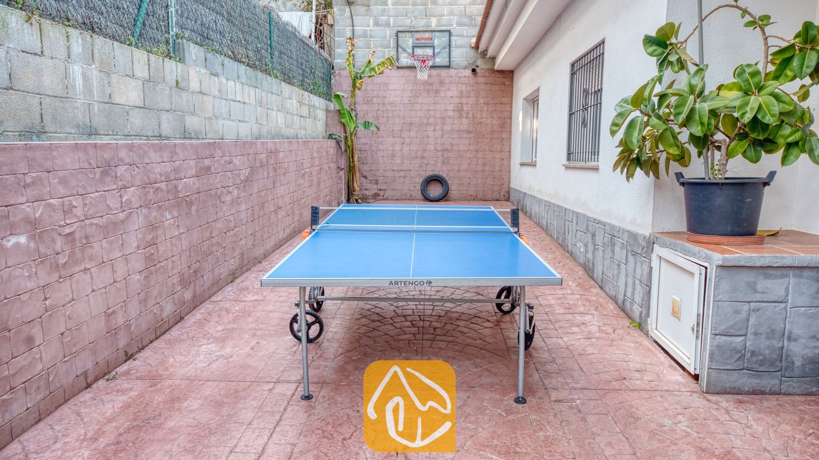 Binnenplaats van Villa Zarita met een blauwe tafeltennistafel op een roodachtig aaneengesloten terras en een basketbalring aan de achtermuur.