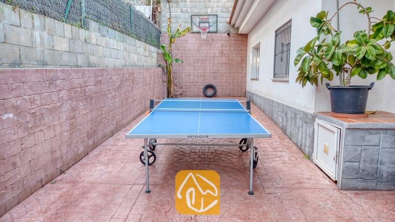 Binnenplaats van Villa Zarita met een blauwe tafeltennistafel op een roodachtig aaneengesloten terras en een basketbalring aan de achtermuur.
