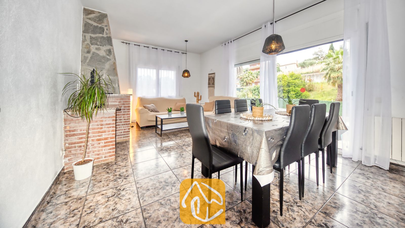 Ruime woon- en eetkamer in Villa Zarita, voorzien van een stenen open haard, plavuizen vloeren, een eettafel met zwarte stoelen en grote ramen met uitzicht op de buitenlucht.