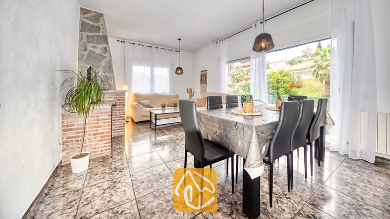 Ruime woon- en eetkamer in Villa Zarita, voorzien van een stenen open haard, plavuizen vloeren, een eettafel met zwarte stoelen en grote ramen met uitzicht op de buitenlucht.