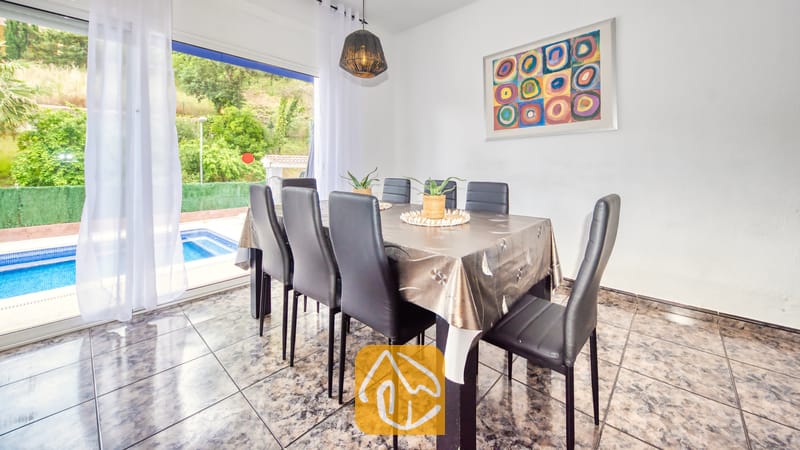 Eetgedeelte in Villa Zarita met een donkere tafel, zwartlederen stoelen, abstracte wanddecoratie en glazen schuifpuien die uitkomen op een zwembadterras.