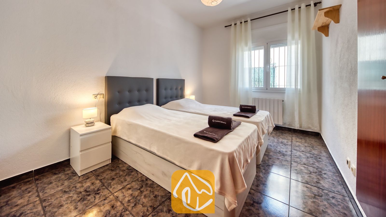 Slaapkamer met twee eenpersoonsbedden, voorzien van donkere gecapitonneerde hoofdborden, lichtbeige spreien en opgevouwen donkere handdoeken bij Villa Zarita.