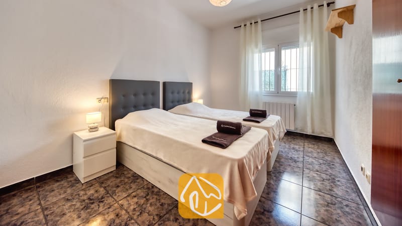 Slaapkamer met twee eenpersoonsbedden, voorzien van donkere gecapitonneerde hoofdborden, lichtbeige spreien en opgevouwen donkere handdoeken bij Villa Zarita.