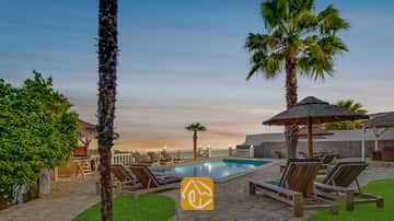 Privé buitenzwembad bij Villa Tropicana, omringd door houten ligstoelen, palmbomen en rieten parasols onder een avondhemel.
