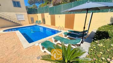 Privé buitenzwembad bij Villa Holiday, omringd door groene ligbedden, een donkere parasol en een stenen terras.