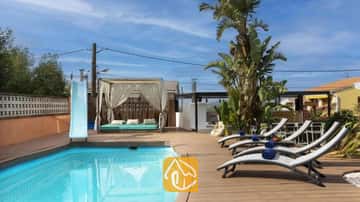 Privézwembad met een blauwe glijbaan, houten terras, grijze ligstoelen met blauwe handdoeken en een gedrapeerde cabana bij Villa Soleia.